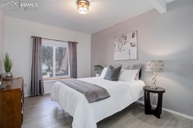 bedroom with baseboards, wood finished floors, and beam ceiling