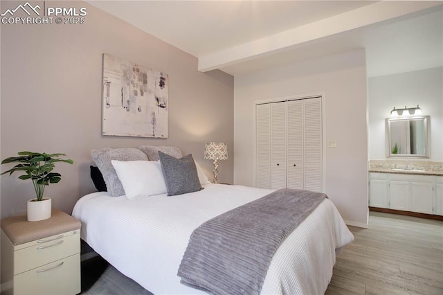 bedroom featuring a closet, beam ceiling, a sink, light wood-style flooring, and ensuite bath