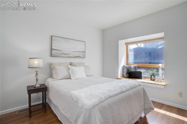 bedroom with baseboards, visible vents, and wood finished floors