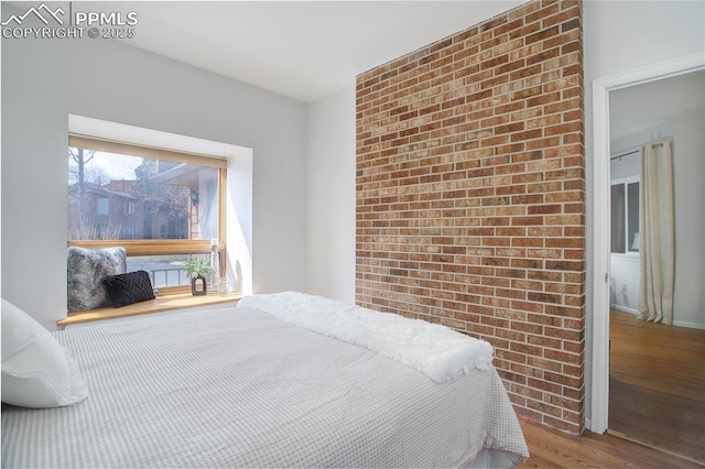 bedroom with wood finished floors and brick wall
