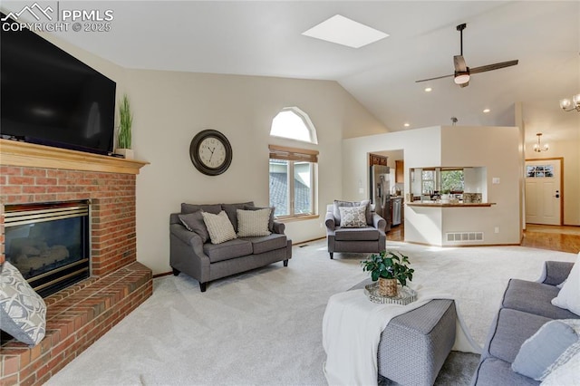 living room with a fireplace, a skylight, ceiling fan with notable chandelier, light colored carpet, and visible vents