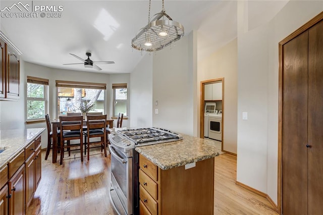 kitchen featuring light wood-style flooring, stainless steel range with gas stovetop, light stone countertops, ceiling fan, and a kitchen island