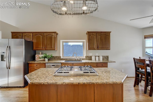 kitchen with stainless steel appliances, a sink, light wood-type flooring, vaulted ceiling, and a notable chandelier