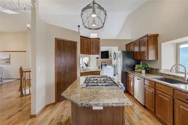 kitchen featuring light wood-type flooring, stainless steel appliances, a center island, a sink, and light stone counters