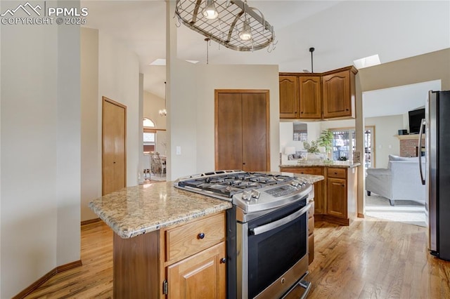 kitchen featuring a kitchen island, light stone countertops, appliances with stainless steel finishes, baseboards, and light wood-style floors