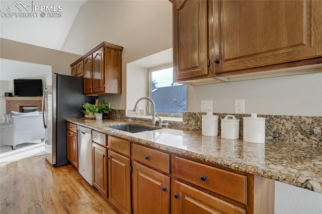 kitchen featuring light stone counters, a sink, appliances with stainless steel finishes, a brick fireplace, and light wood-style floors
