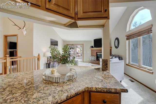 kitchen with a brick fireplace, light stone counters, light colored carpet, and brown cabinets