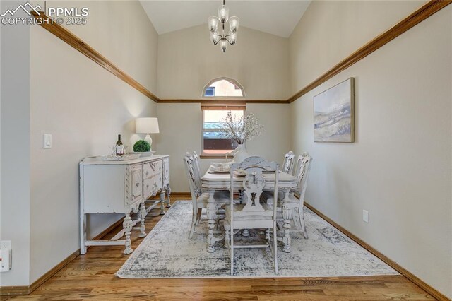 dining area with baseboards, high vaulted ceiling, wood finished floors, and an inviting chandelier