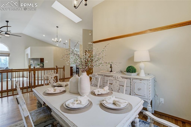 dining space with high vaulted ceiling, a skylight, baseboards, light wood-style floors, and ceiling fan with notable chandelier