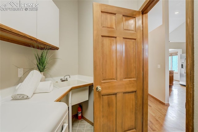 washroom featuring baseboards, cabinet space, a sink, and light wood-type flooring