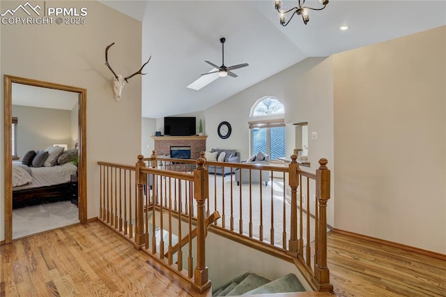 corridor with vaulted ceiling with skylight, wood finished floors, an upstairs landing, and baseboards