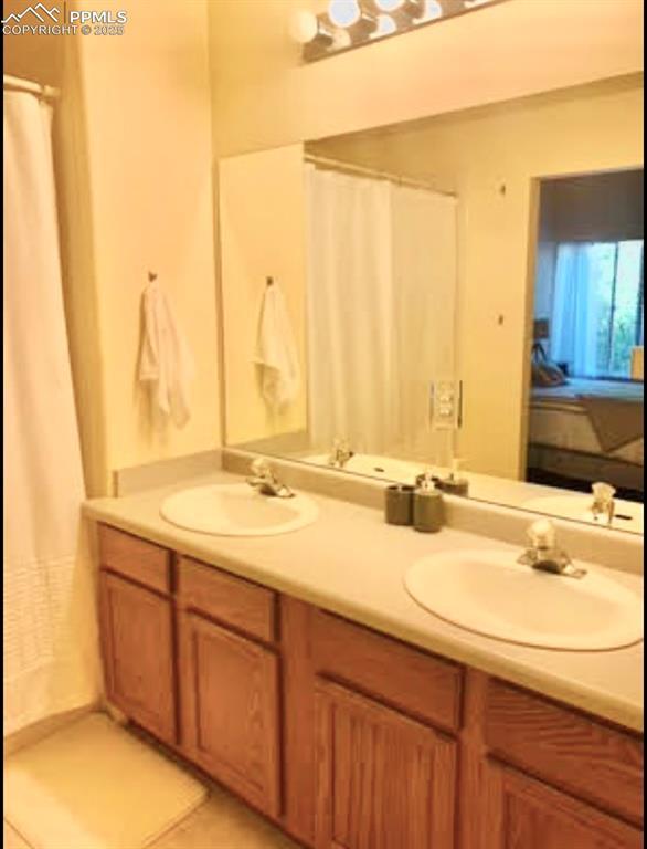 full bathroom with double vanity, connected bathroom, and a sink