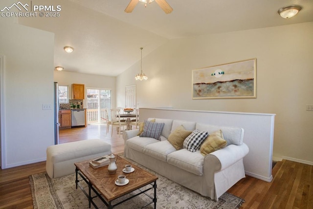 living room featuring ceiling fan with notable chandelier, lofted ceiling, wood finished floors, and baseboards