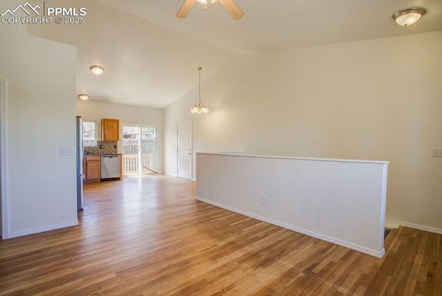 spare room with ceiling fan with notable chandelier, vaulted ceiling, wood finished floors, and baseboards