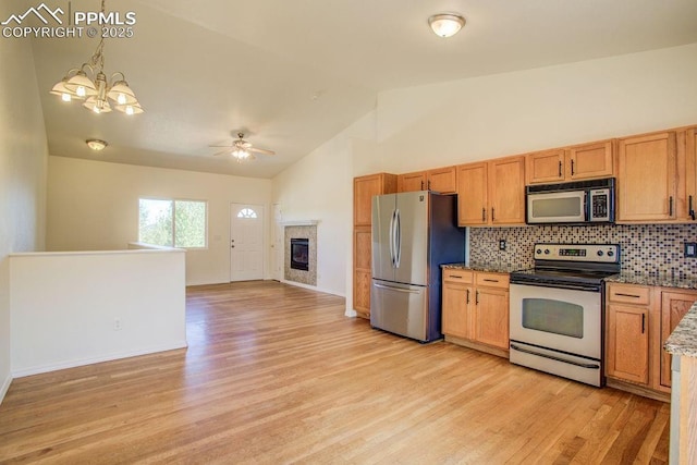 kitchen with open floor plan, light wood-style floors, appliances with stainless steel finishes, a tiled fireplace, and tasteful backsplash