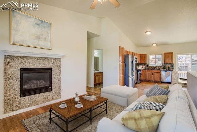 living area featuring baseboards, vaulted ceiling, a fireplace, and light wood finished floors