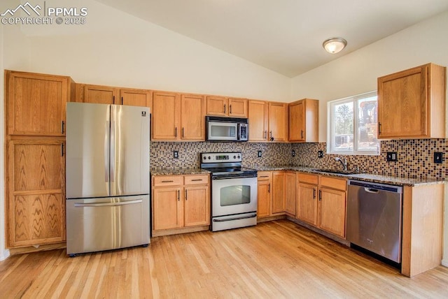 kitchen featuring a sink, stainless steel appliances, dark stone counters, and vaulted ceiling