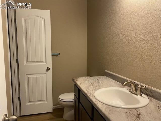 bathroom with vanity, wood finished floors, toilet, and a textured wall