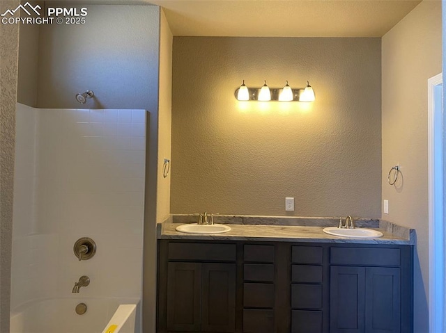 bathroom with double vanity, a textured wall,  shower combination, and a sink