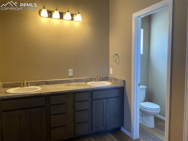 full bathroom with double vanity, wood finished floors, toilet, and a sink