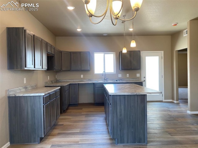 kitchen featuring visible vents, a kitchen island, wood finished floors, and a sink