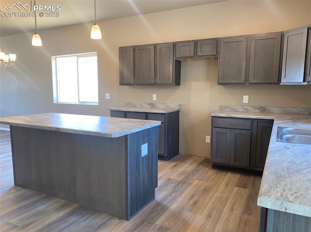 kitchen featuring pendant lighting, light wood-style flooring, a sink, a kitchen island, and light countertops