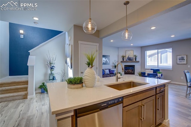 kitchen with light wood finished floors, open floor plan, stainless steel dishwasher, a glass covered fireplace, and a sink