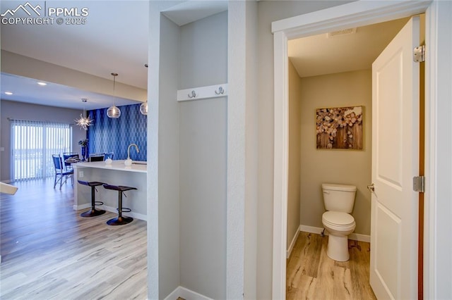 bathroom featuring visible vents, baseboards, toilet, wood finished floors, and a sink