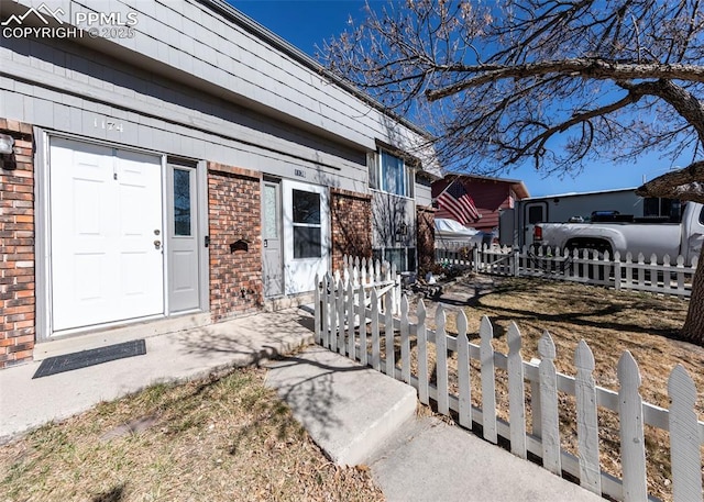 view of exterior entry featuring brick siding and fence