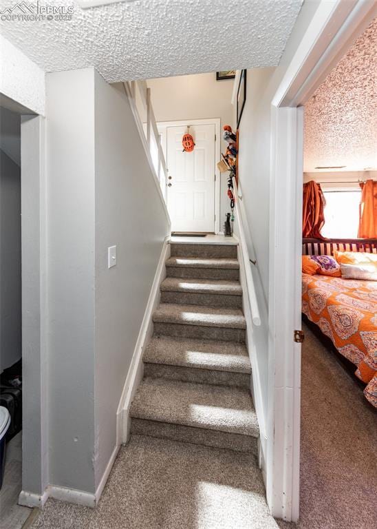 staircase featuring baseboards, a textured ceiling, and carpet flooring