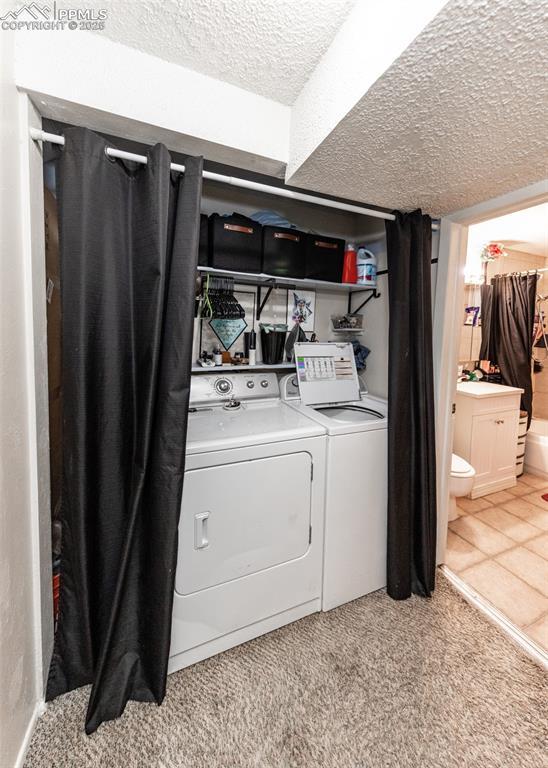 washroom featuring laundry area, light carpet, washer and clothes dryer, and a textured ceiling