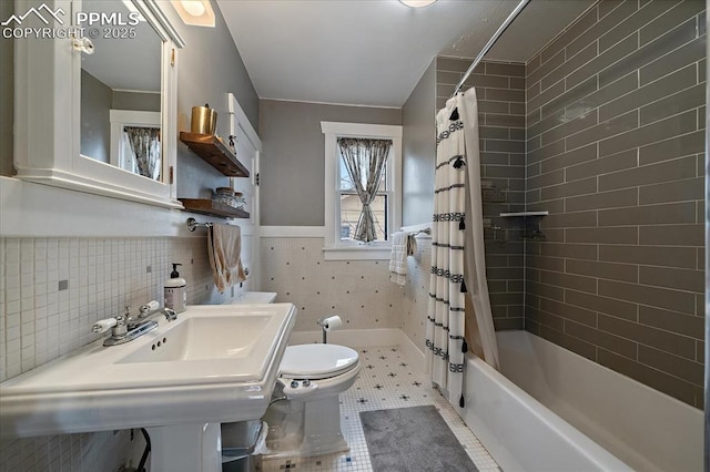 bathroom featuring tile patterned floors, toilet, tile walls, shower / tub combo, and wainscoting