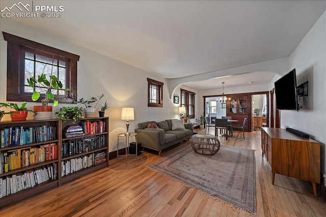 living area featuring a notable chandelier, arched walkways, and light wood-type flooring