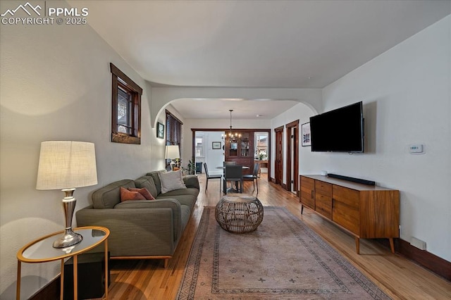 living room with arched walkways, a chandelier, light wood-style flooring, and baseboards