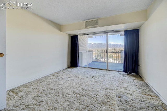 carpeted empty room with visible vents, baseboards, a textured ceiling, and a mountain view