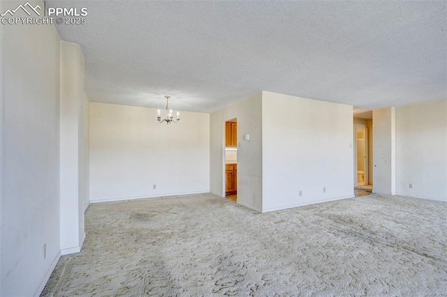 unfurnished room featuring light carpet, baseboards, a textured ceiling, and an inviting chandelier