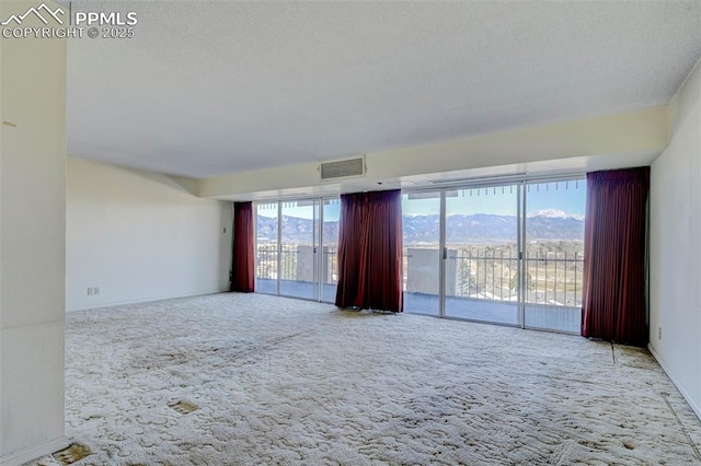 carpeted empty room featuring visible vents, a mountain view, and a textured ceiling