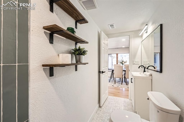 bathroom featuring visible vents, toilet, vanity, and a textured wall