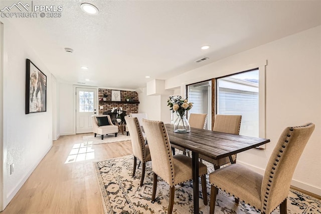 dining room featuring visible vents, light wood-style flooring, a textured ceiling, a fireplace, and baseboards