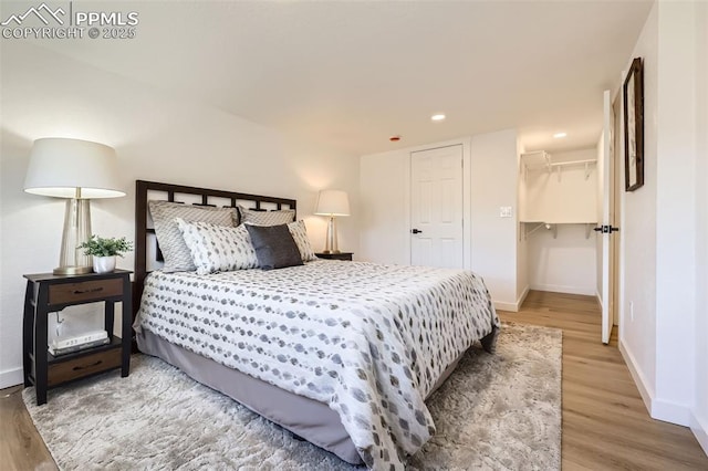 bedroom with a spacious closet, recessed lighting, baseboards, and wood finished floors