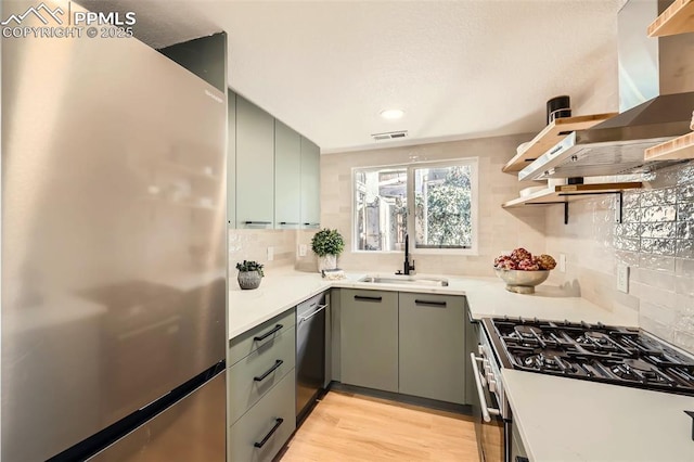 kitchen with visible vents, a sink, light wood-style floors, appliances with stainless steel finishes, and wall chimney exhaust hood