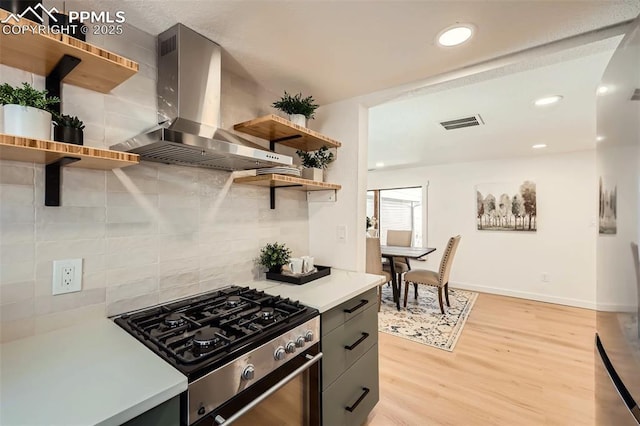 kitchen with open shelves, wall chimney exhaust hood, light countertops, and gas range