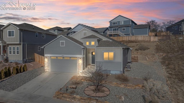 view of front facade with board and batten siding, concrete driveway, an attached garage, and fence