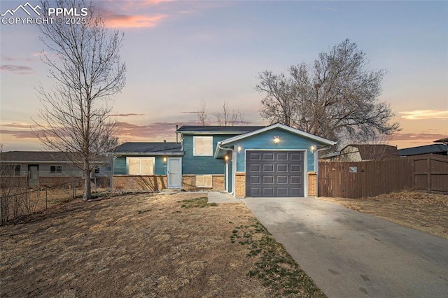 view of front of property featuring brick siding, an attached garage, driveway, and fence