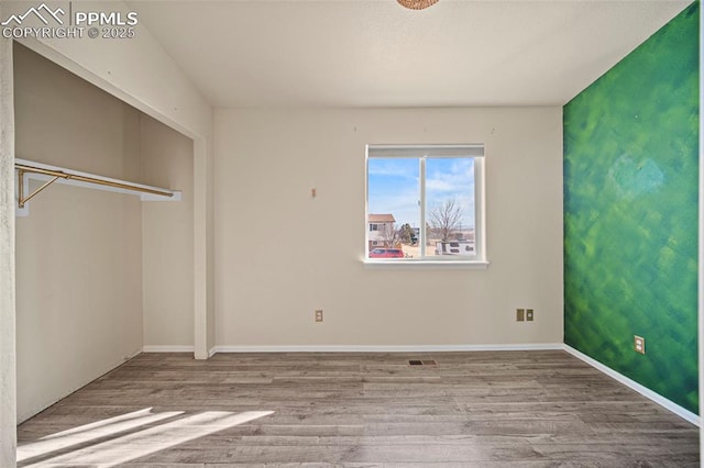 unfurnished bedroom with visible vents, wood finished floors, baseboards, and a closet