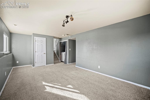 carpeted empty room featuring visible vents, baseboards, stairs, a textured wall, and washer and dryer