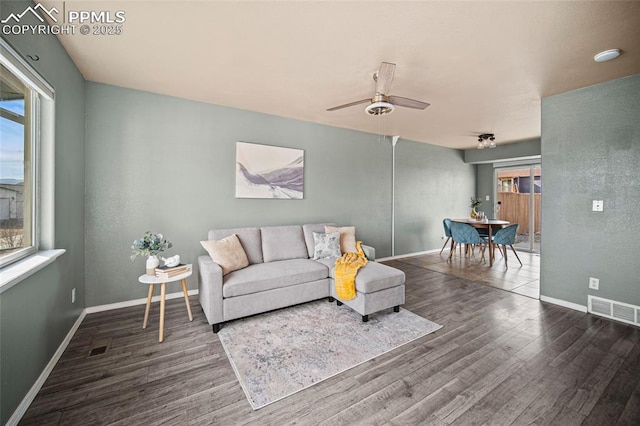 living room featuring a ceiling fan, wood finished floors, visible vents, and baseboards