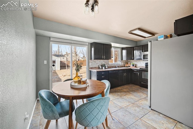 kitchen with backsplash, light countertops, a textured wall, black appliances, and a sink