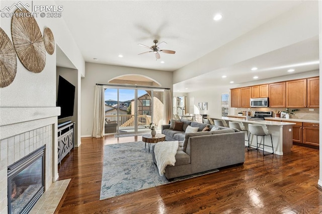 living area with dark wood-style floors, recessed lighting, a tiled fireplace, and ceiling fan