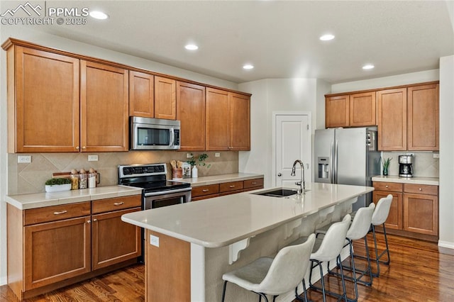 kitchen with a breakfast bar, a sink, tasteful backsplash, stainless steel appliances, and dark wood-style flooring